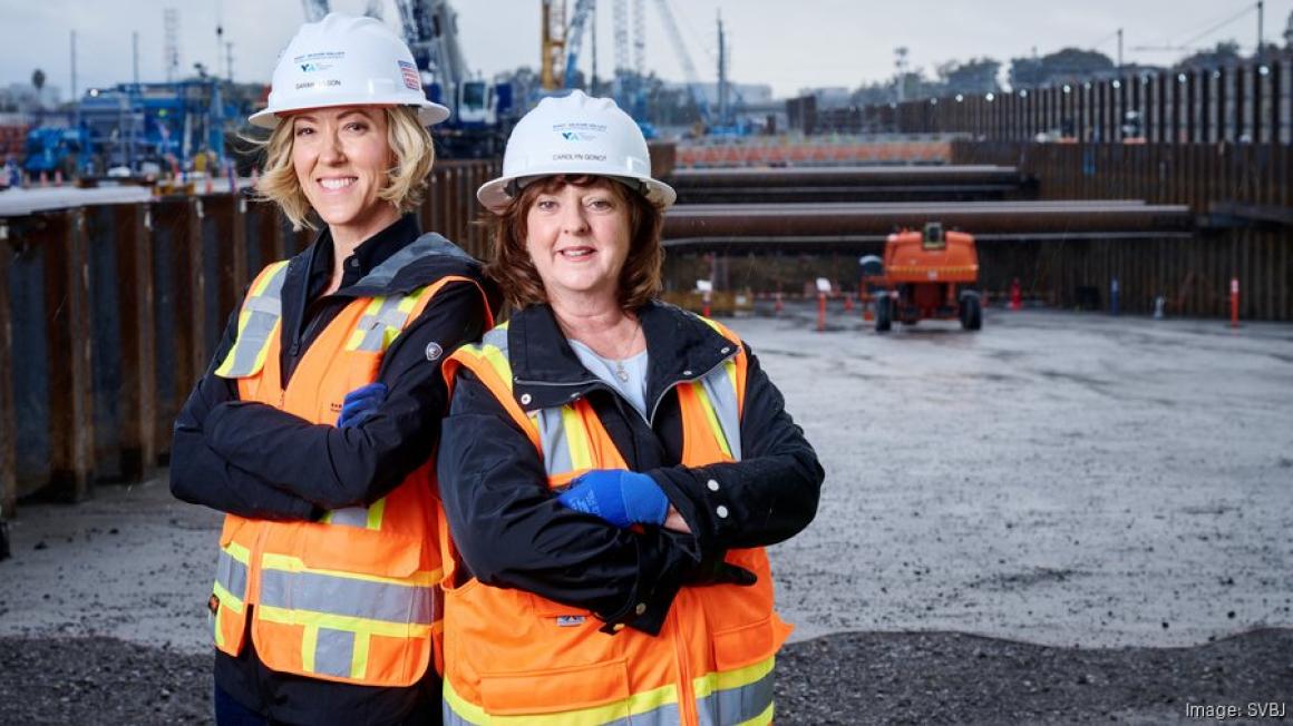 Two women posing for a photo at a construction site, wearing PPE