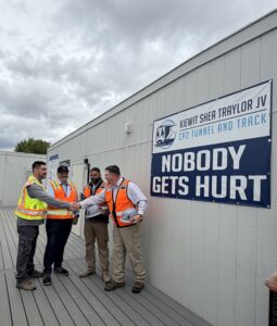 Construction workers shake hands with a poster behind them that says "Nobody Gets Hurt"
