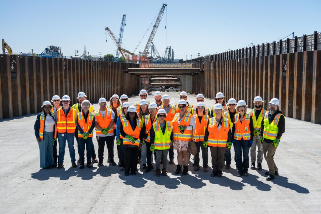 A group of people wearing construction hats and safety vest pose for a group photo at the BSVII construction site.