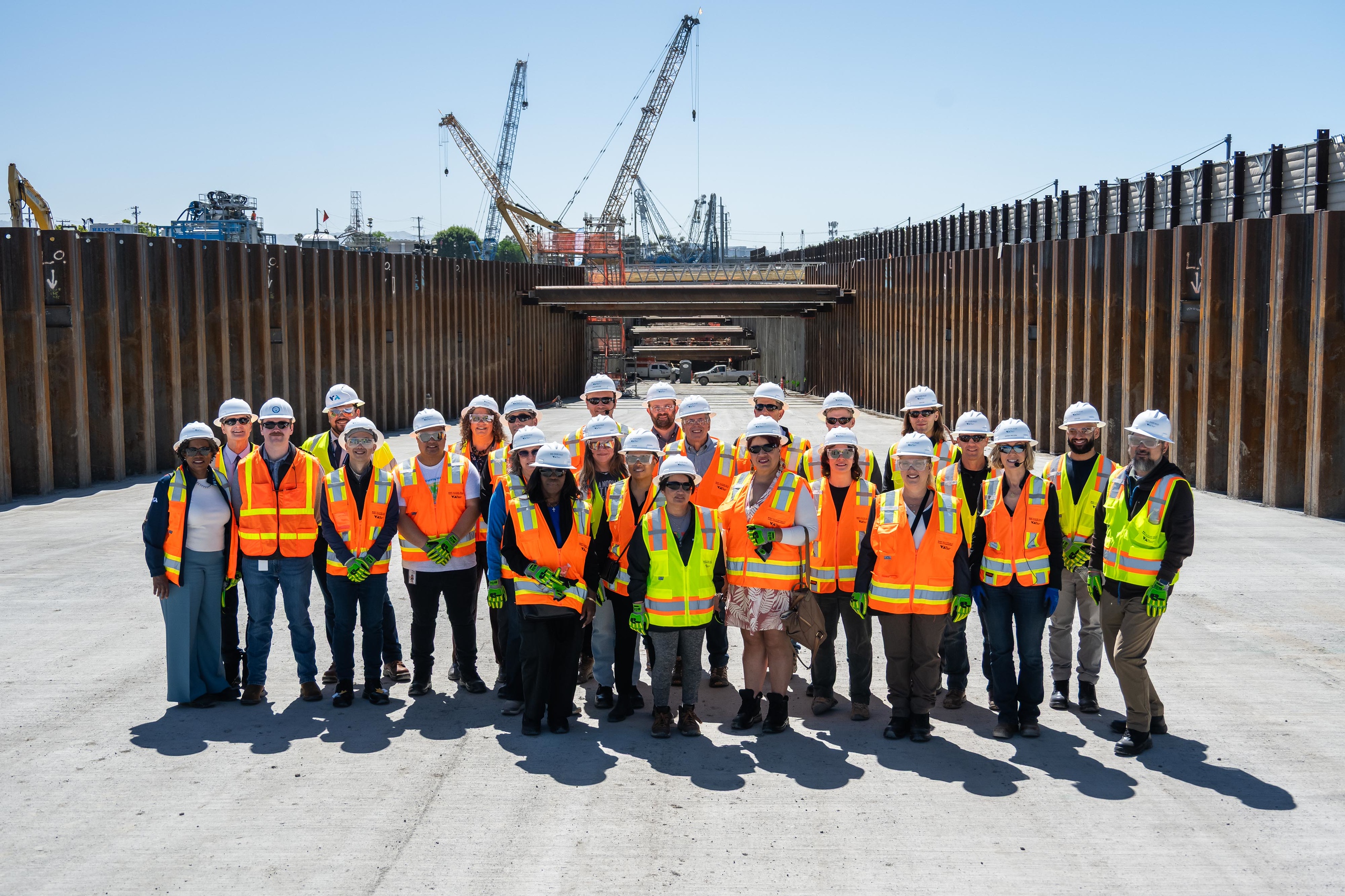 A group of people wearing construction hats and safety vest pose for a group photo at the BSVII construction site.