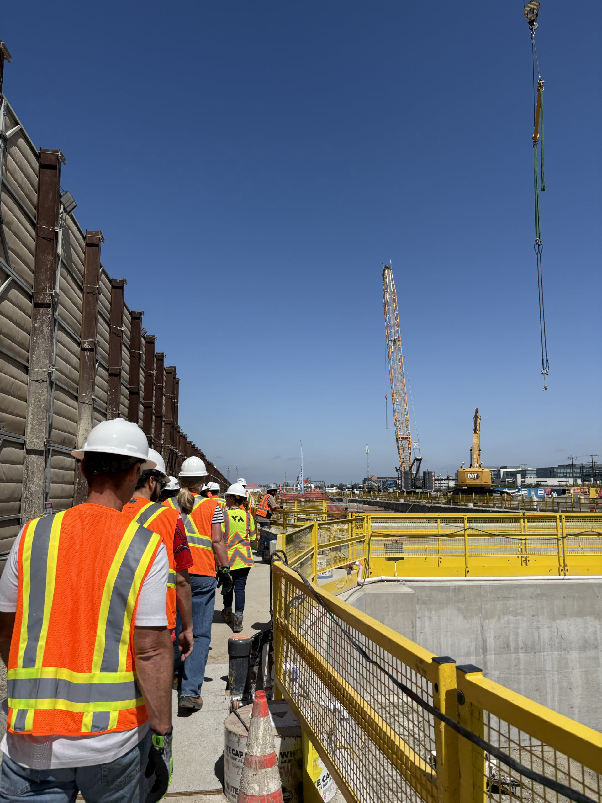 A group of people in construction PPE walk on the perimeter of a construction site