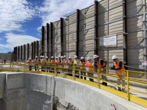 People wearing construction gear look over a gate peering into a hole at a construction site