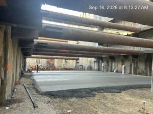 In a construction site with tall cement walls and large metal bearing struts across the walls