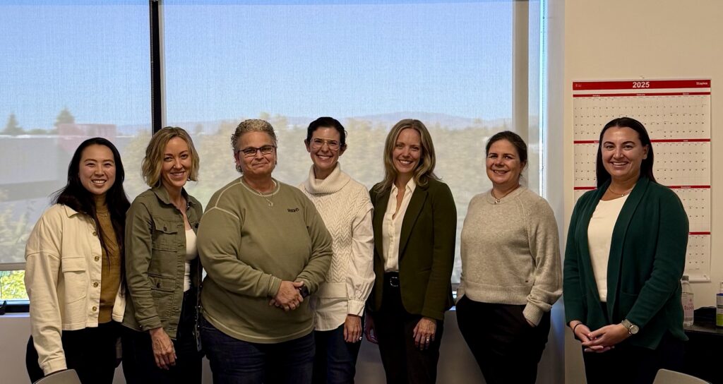 Seven women pose for a photo in an office setting